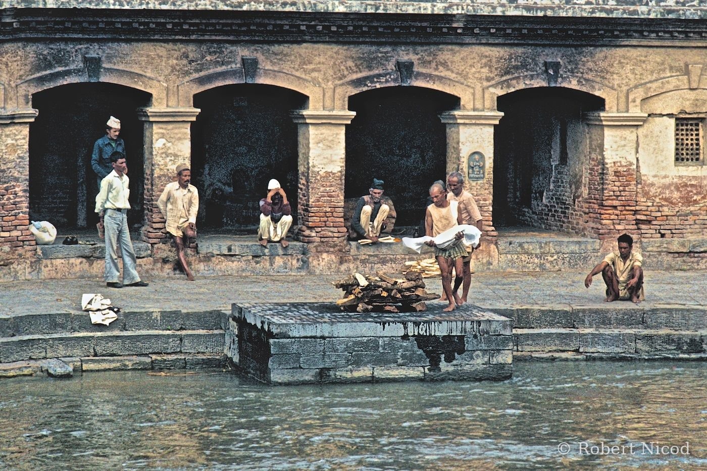 Reportage Népal 1977 — Préparatifs funéraires d'un enfant de huit ans. À droite, son père accroupi, le regard vers le sol, Pashupatinath 1977